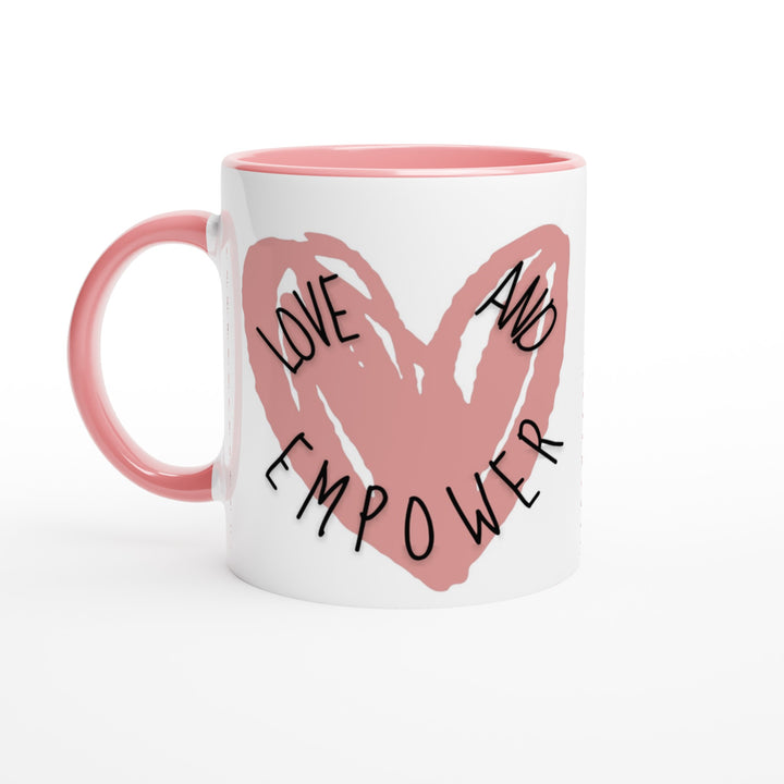 A white ceramic mug with a pink interior and handle, adorned with a large, hand-drawn pink heart and the words ‘LOVE AND EMPOWER’ in bold black lettering across it.